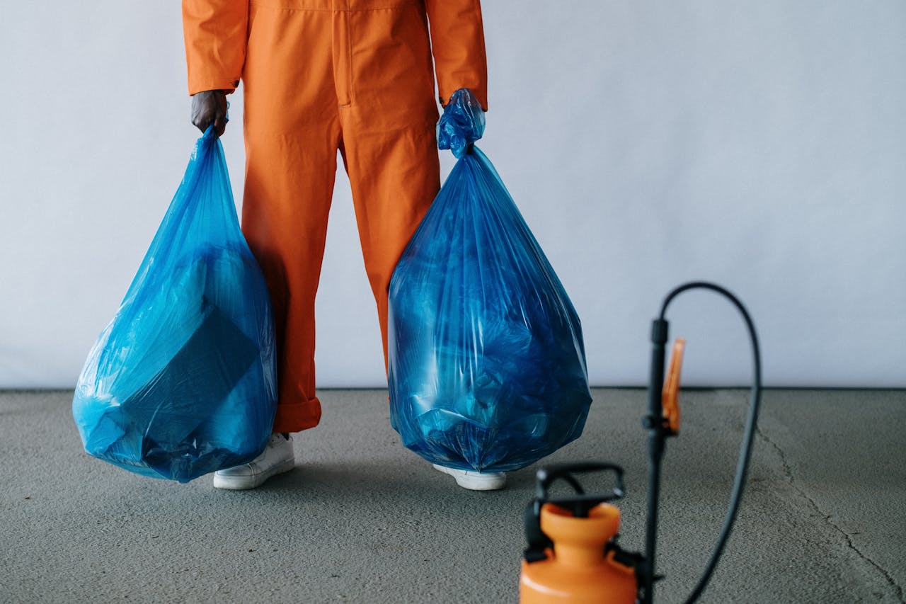 services-03 Sanitation worker in orange overalls holding blue trash bags indoors for waste management.